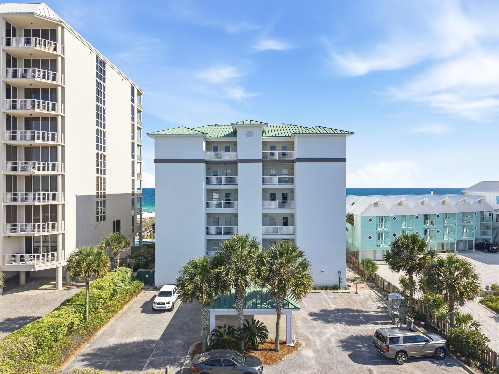 A multi-story hotel with balconies, a parking area, and palm trees.