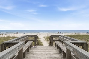 Une promenade en bois qui mÚne à une plage, avec un ciel dégagé.