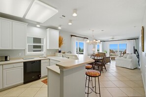 A modern kitchen with white cabinetry, a dishwasher, and a bar area with stools. - Riviera Dunes 201 (Pensacola)