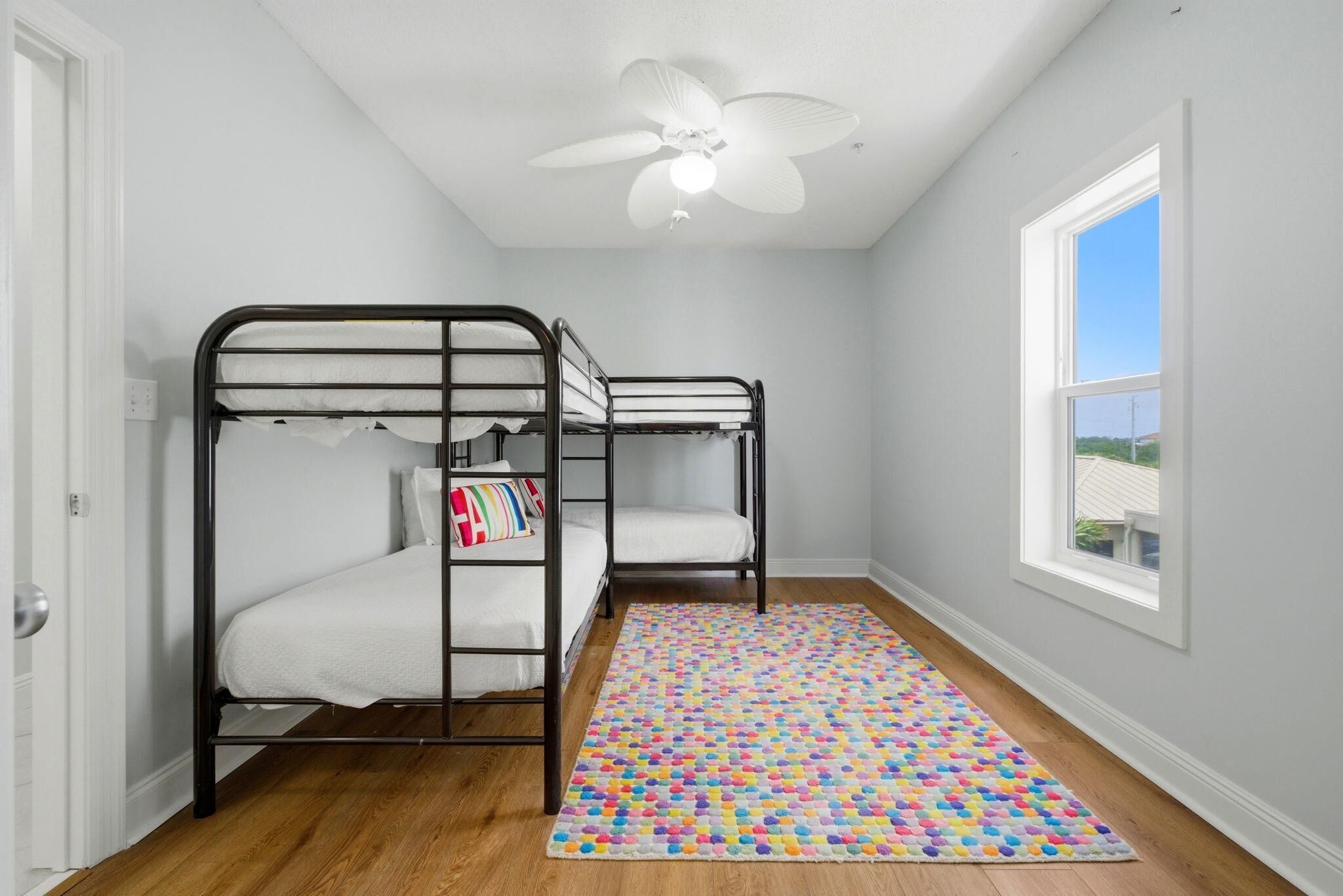 A room with bunk beds, a ceiling fan, a window with a view, and a colorful rug.