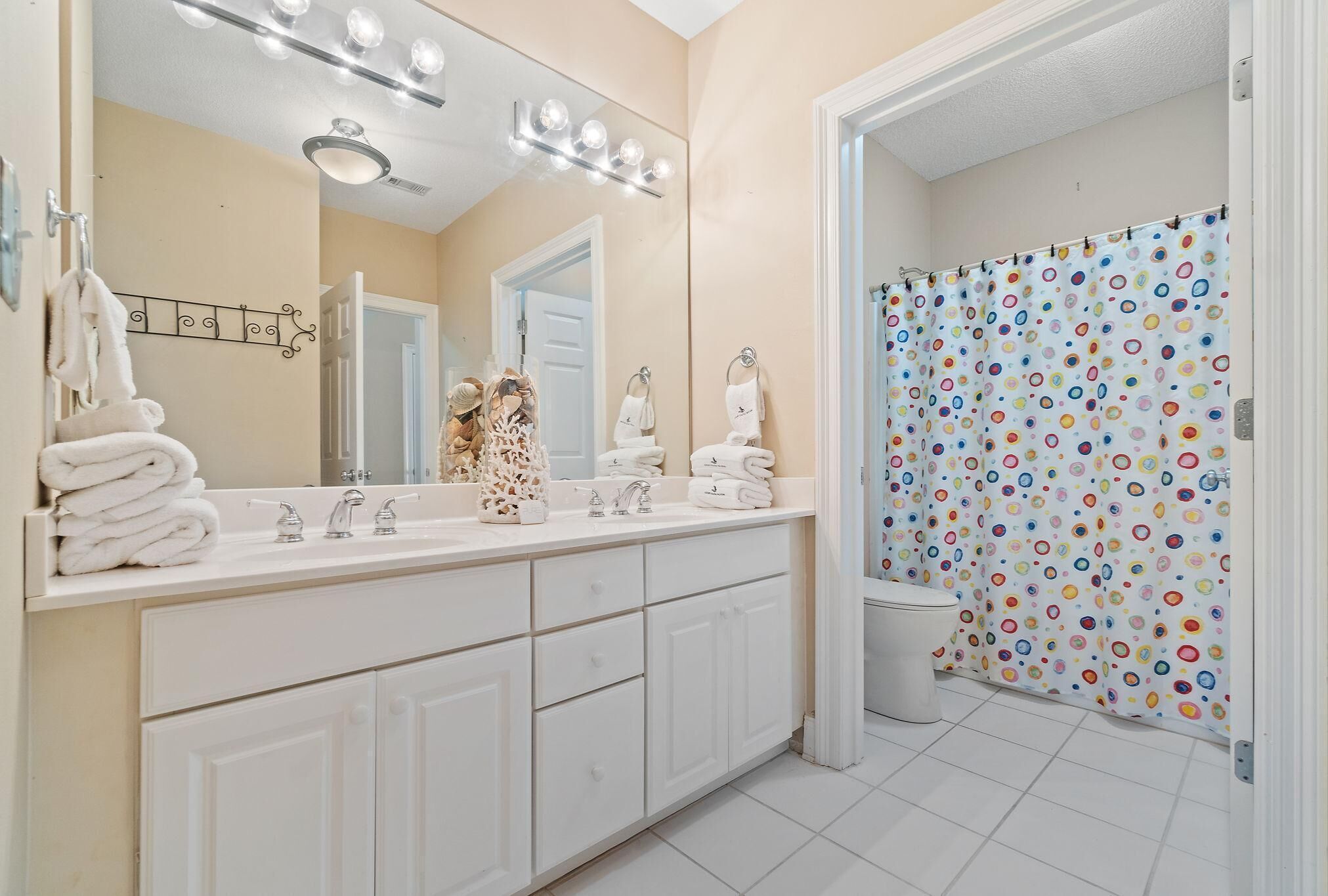 A bathroom with a double sink, a large mirror, and a shower curtain with a polka dot pattern.