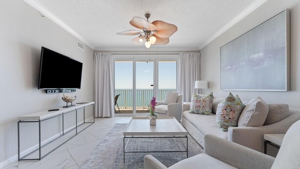 Uma sala de estar moderna com televisão de tela plana, ventilador de teto, janela grande com vista e sofá com almofadas florais.