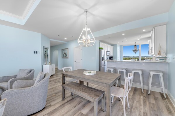 A modern kitchen with a central island, white bar stools, and a view to the outside. - La Playa 701 (Pensacola)
