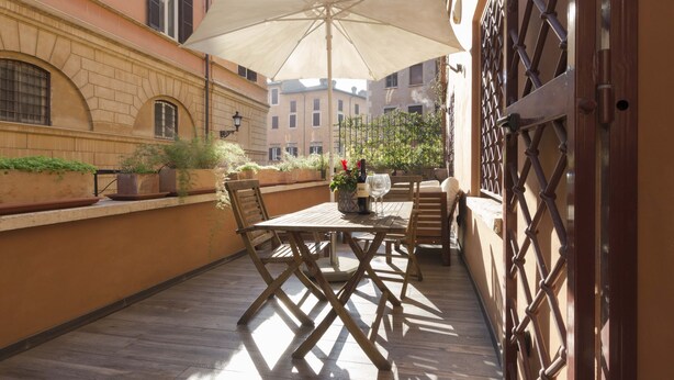 Un patio al aire libre con una mesa y sillas de madera, un paraguas grande y plantas en macetas.