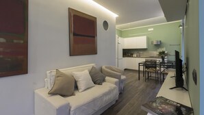 Una sala de estar moderna con un sofá blanco, un comedor con una mesa y sillas, y una cocina al fondo.