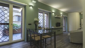 Un comedor con una mesa y sillas de vidrio, un jarrón con flores y vistas al patio exterior a través de un ventanal corredero.