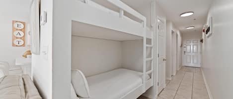 A bunk bed room with a white color scheme, a beige sofa, and a wall-mounted sign that says "EAT".