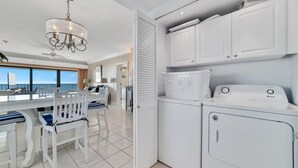 Una cuina moderna amb armaris blancs, rentadora i assecadora integrades, una làmpada penjant i una zona de menjador amb vistes.