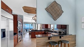 A modern kitchen with wooden cabinets, a large island, and bar stools. - Indigo East 2104 Penthouse (Pensacola)