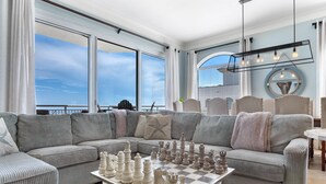 A modern living room with a large chessboard, a sofa, and a view of the sea. - Indigo East 2104 Penthouse (Pensacola)