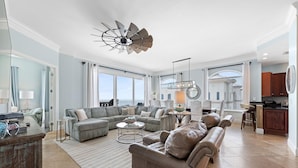 A spacious living room with a large sectional sofa, a coffee table, and a fireplace. There is a kitchen area with a dining table and chairs. - Indigo East 2104 Penthouse (Pensacola)