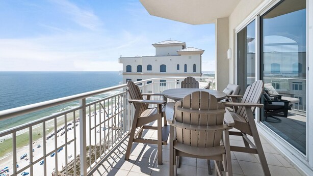 A balcony with a table and chairs overlooking a beach and ocean. - Indigo East 2104 Penthouse (Pensacola)