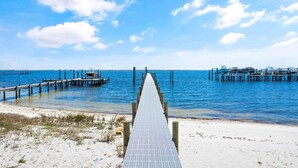 A pier leading to a dock with boats, extending into a calm sea under a clear sky.