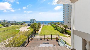 A balcony with a view of a marina, a grassy area, and a tall building in the background.