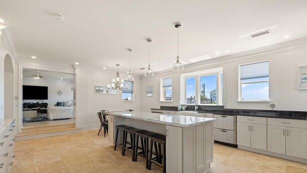 A modern kitchen with a large island, bar stools, pendant lights, and a view of the outdoors.