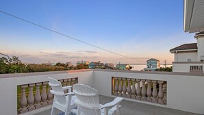 A balcony with two white chairs, a patterned rug, and a view of houses in the distance.