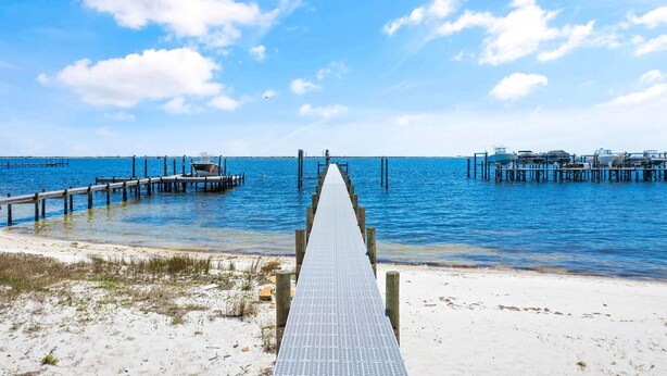 A pier leading to a dock with boats, extending into a calm sea under a clear sky.