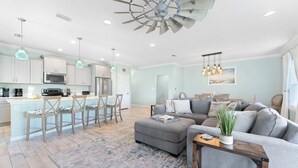 A modern living room with a gray sectional sofa, a wooden coffee table, and a dining area with a light blue island and bar stools.