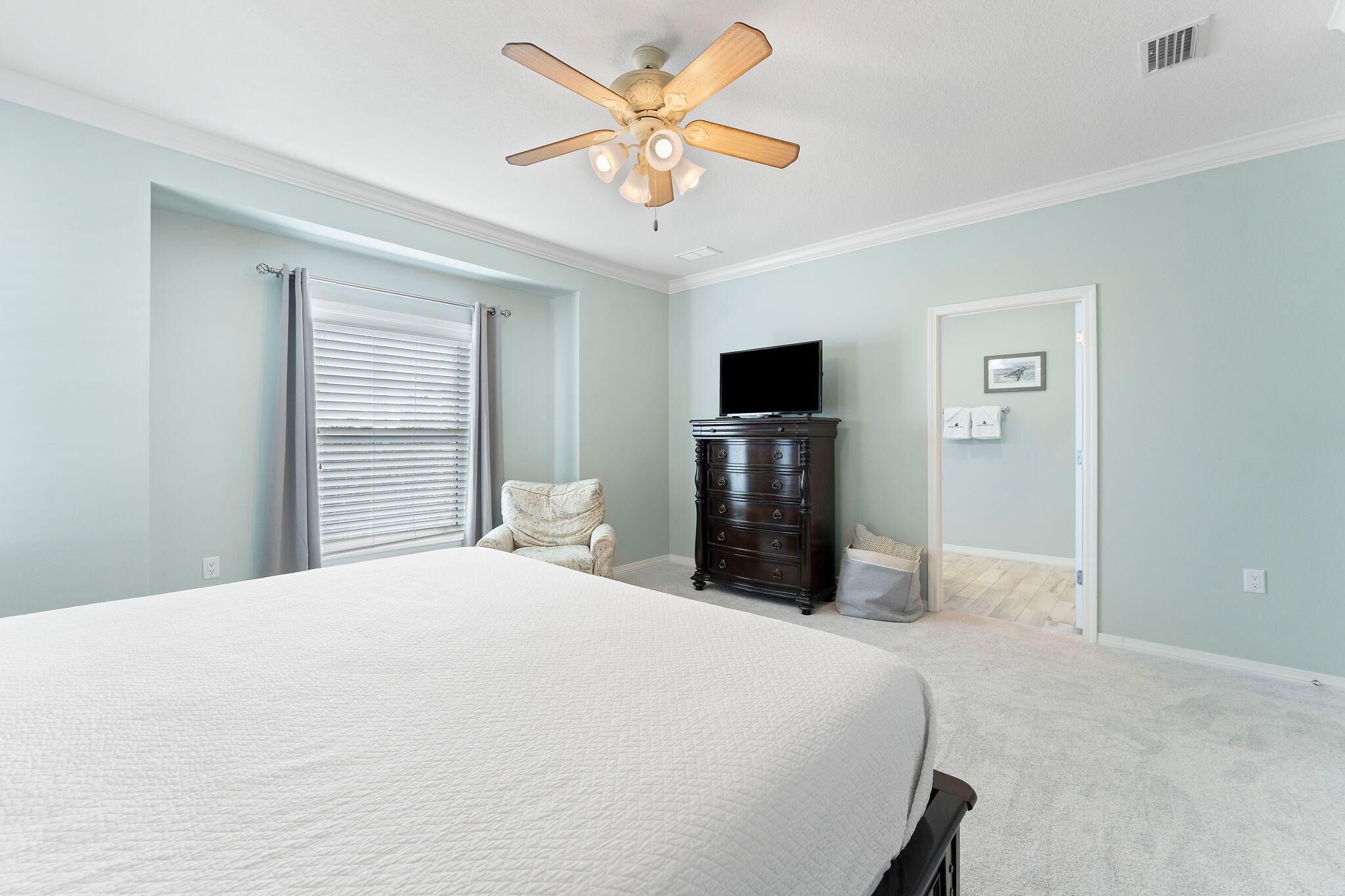 A bedroom with a bed, a dresser, a television, and a ceiling fan.