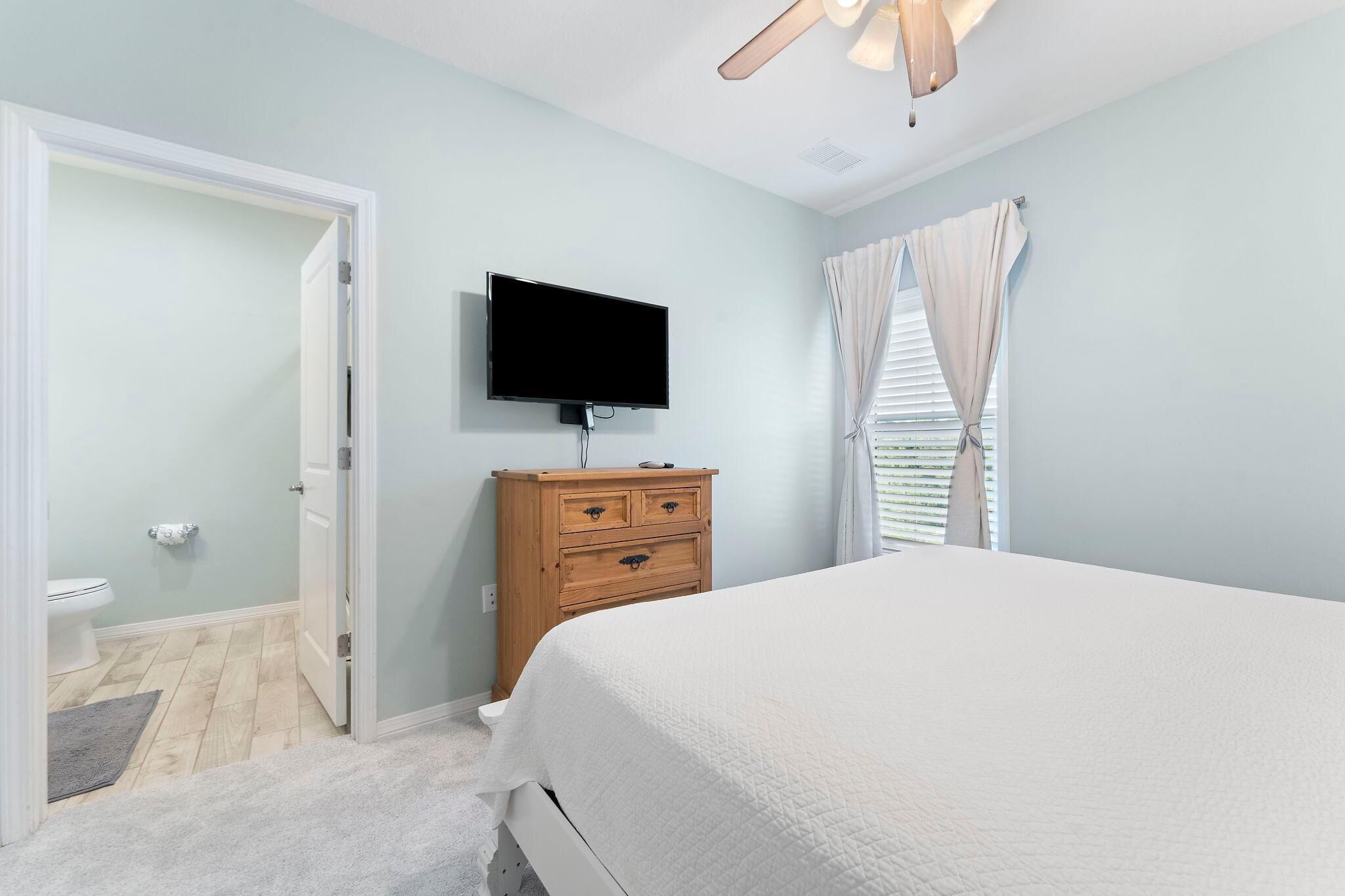 Une chambre à coucher comprenant un lit, une commode en bois, un téléviseur et une porte donnant sur une salle de bain.