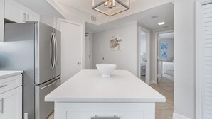 A modern kitchen with a stainless steel refrigerator, a white countertop, and a decorative light fixture. - Summer House 1203a (Orange Beach)