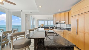 A modern kitchen with a large island, wooden cabinets, and a view of the ocean. - Mediterranean East 1101 (Pensacola)