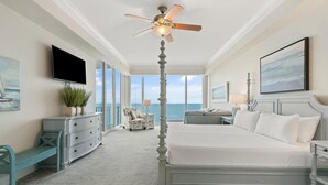 A bedroom with a large bed, a ceiling fan, a TV, a view of the ocean, and a potted plant. - Mediterranean East 1101 (Pensacola)