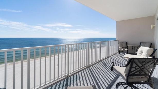 Un balcon avec vue sur la plage et l’océan, comprenant deux chaises et une petite table.