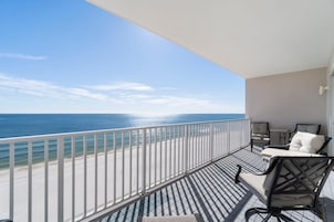 A balcony with a view of the beach and ocean, featuring two chairs and a small table.