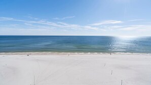 Une vaste plage de sable fin, sous un ciel bleu dégagé et avec une mer calme.
