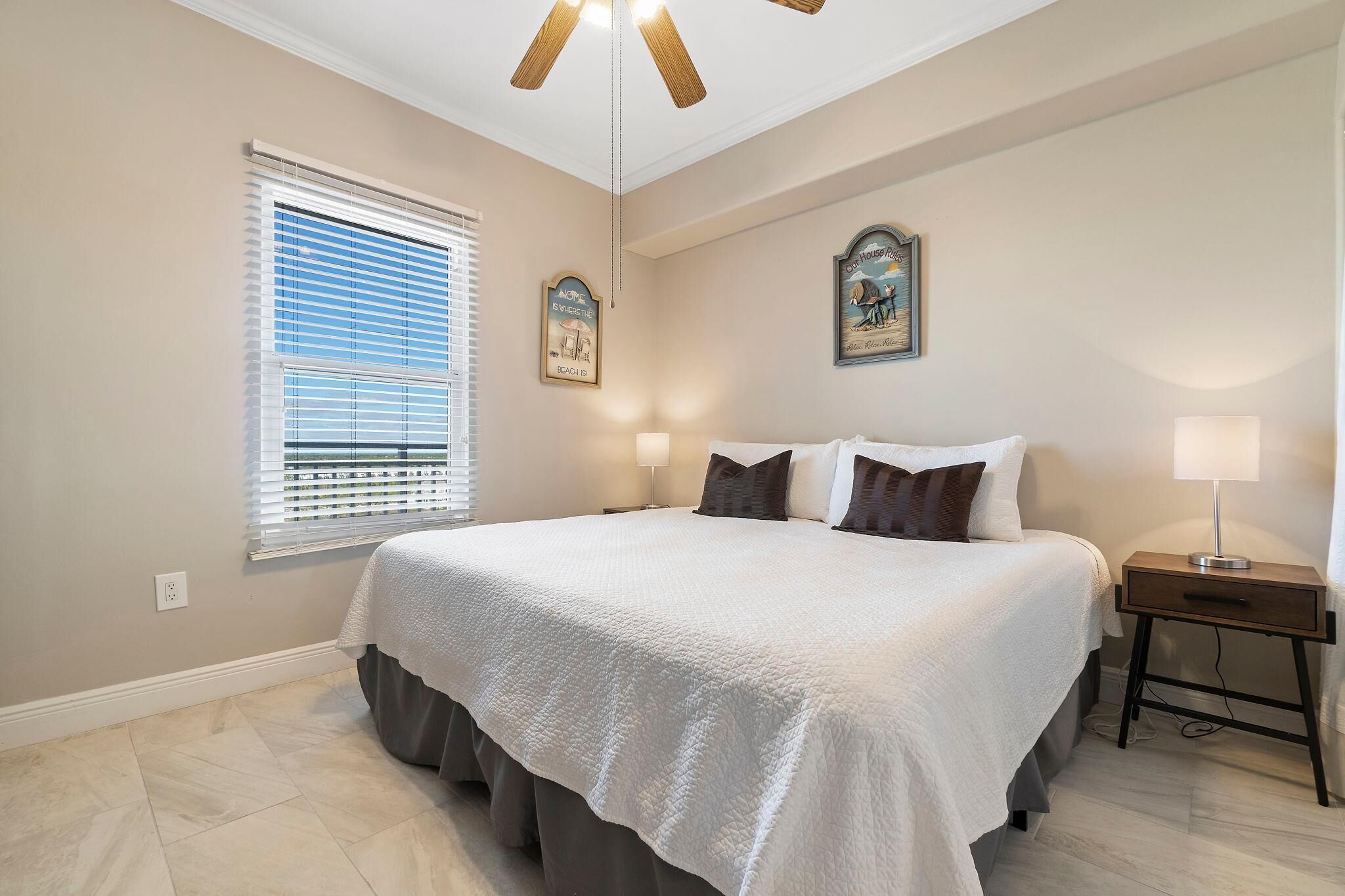 A bedroom with a large bed, two bedside lamps, a nightstand, and a ceiling fan.