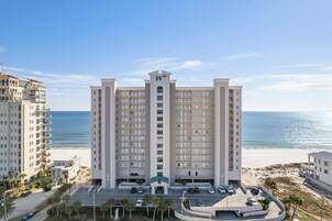 A high-rise hotel with multiple balconies, a central entrance, and a view of the beach.