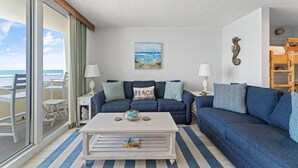 A living room with a beach view, a sofa, a coffee table, and a painting of the beach. - Perdido Sun 502 (Pensacola)