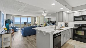 A modern kitchen with a central island, a dining area with a view, and a living room with a sofa and a TV. - Perdido Sun 706 (Pensacola)