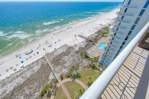 A beach view from a balcony overlooking a hotel with a pool and beach chairs.