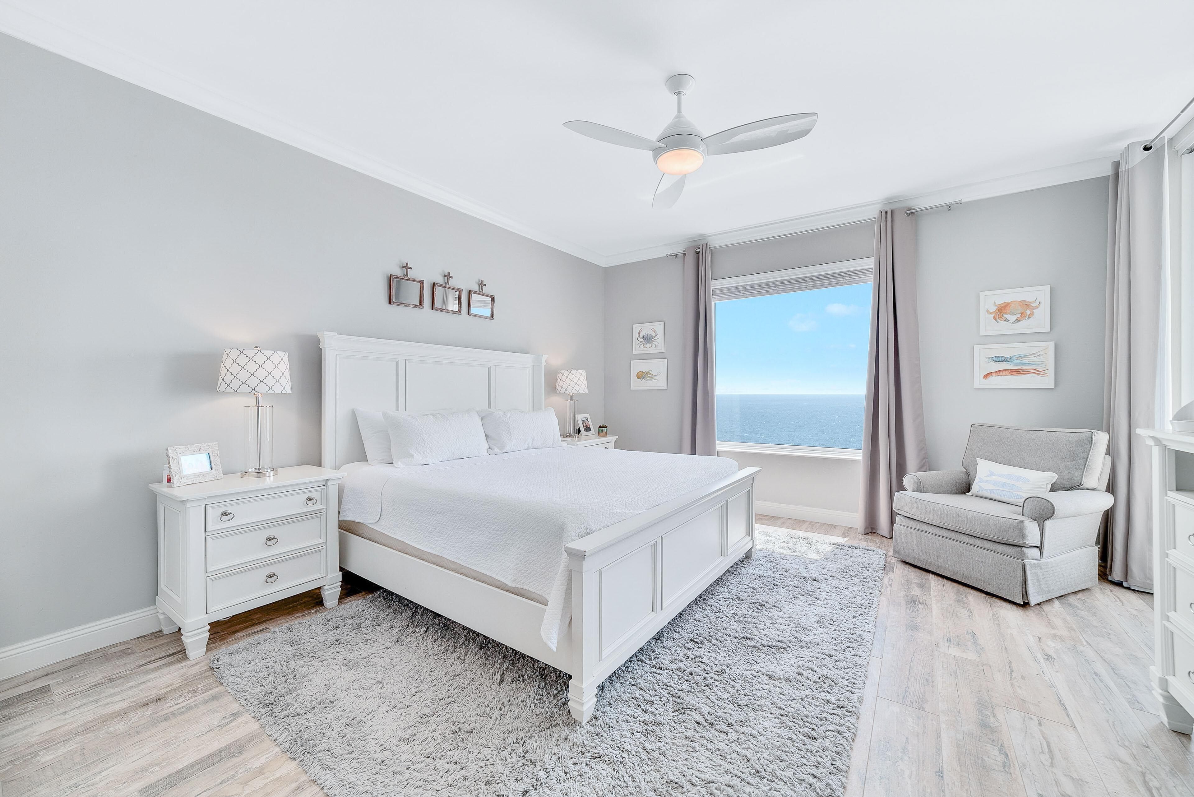 A bedroom with a bed, nightstands, a chair, a ceiling fan, and a window with a view.
