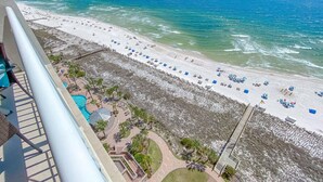 Une vue sur la plage depuis un balcon, avec une piscine, des parasols et des chaises longues.