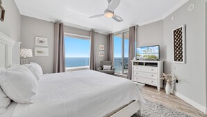 Une chambre avec un grand lit, un ventilateur de plafond, une télévision et une vue sur l’océan.