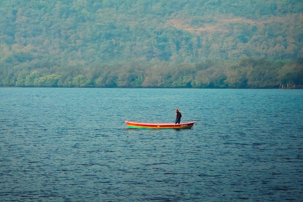 Un lago tranquilo con una sola embarcación y una colina boscosa al fondo.