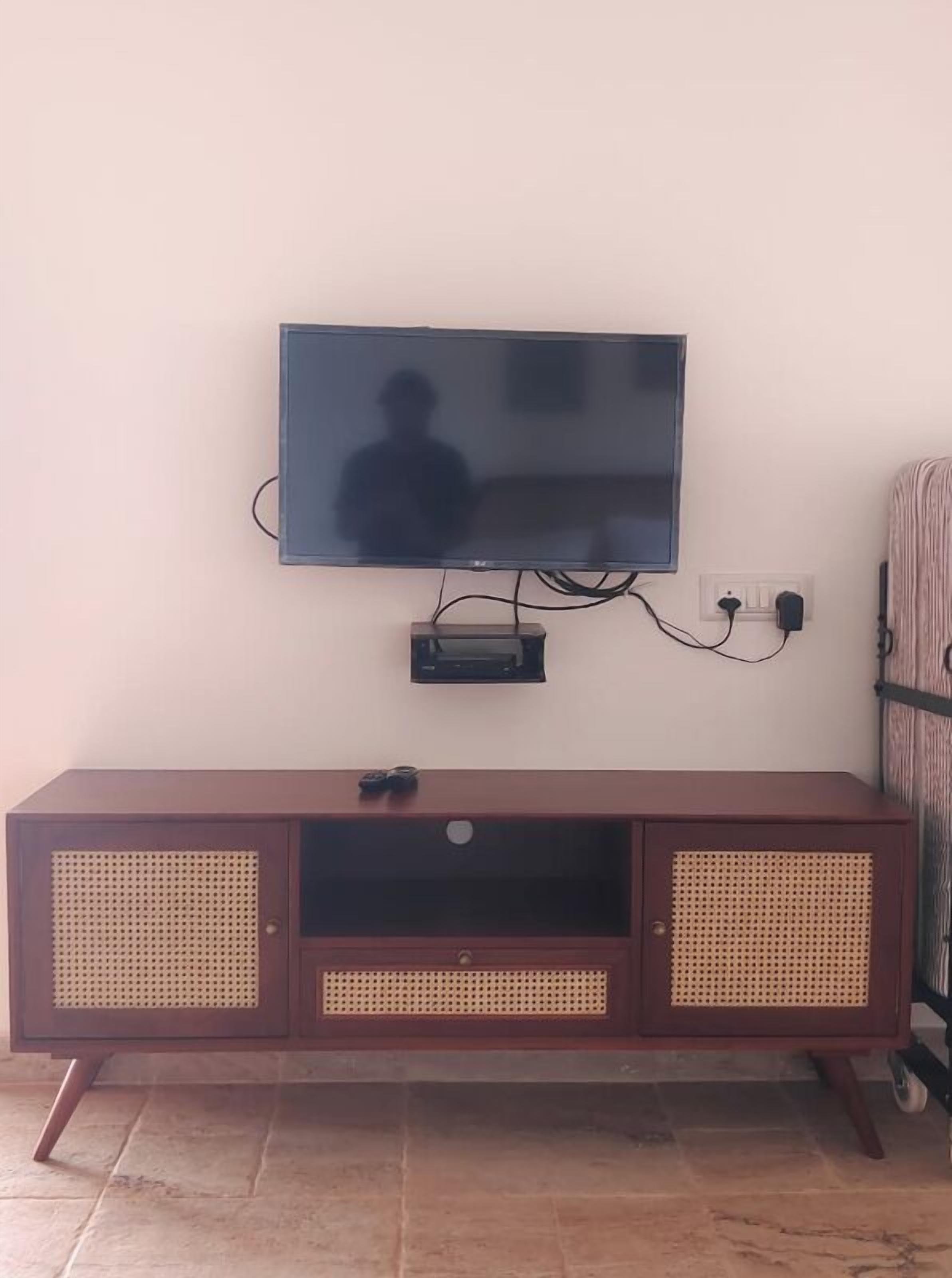 A television mounted on a wall above a wooden entertainment unit with a speaker.