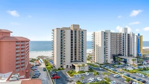 Un hotel frente a la playa con varios edificios altos, un estacionamiento y vista al océano.