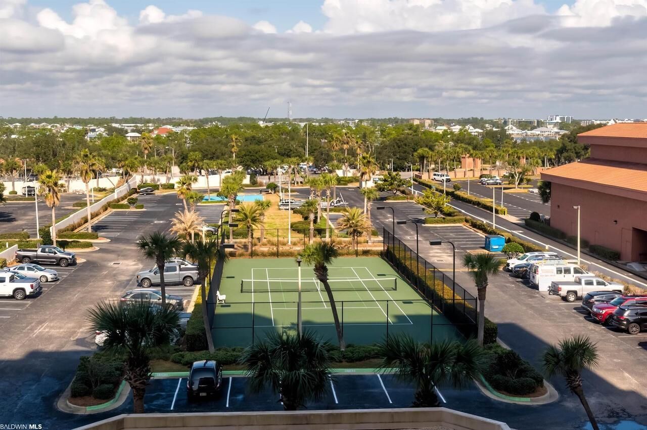 A parking lot with a tennis court, surrounded by palm trees and buildings.