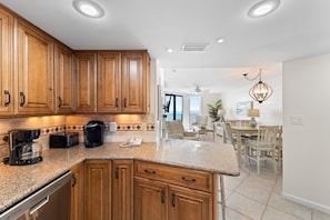 Una cocina con armarios de madera, encimera de granito, cafetera y comedor con candelabro.