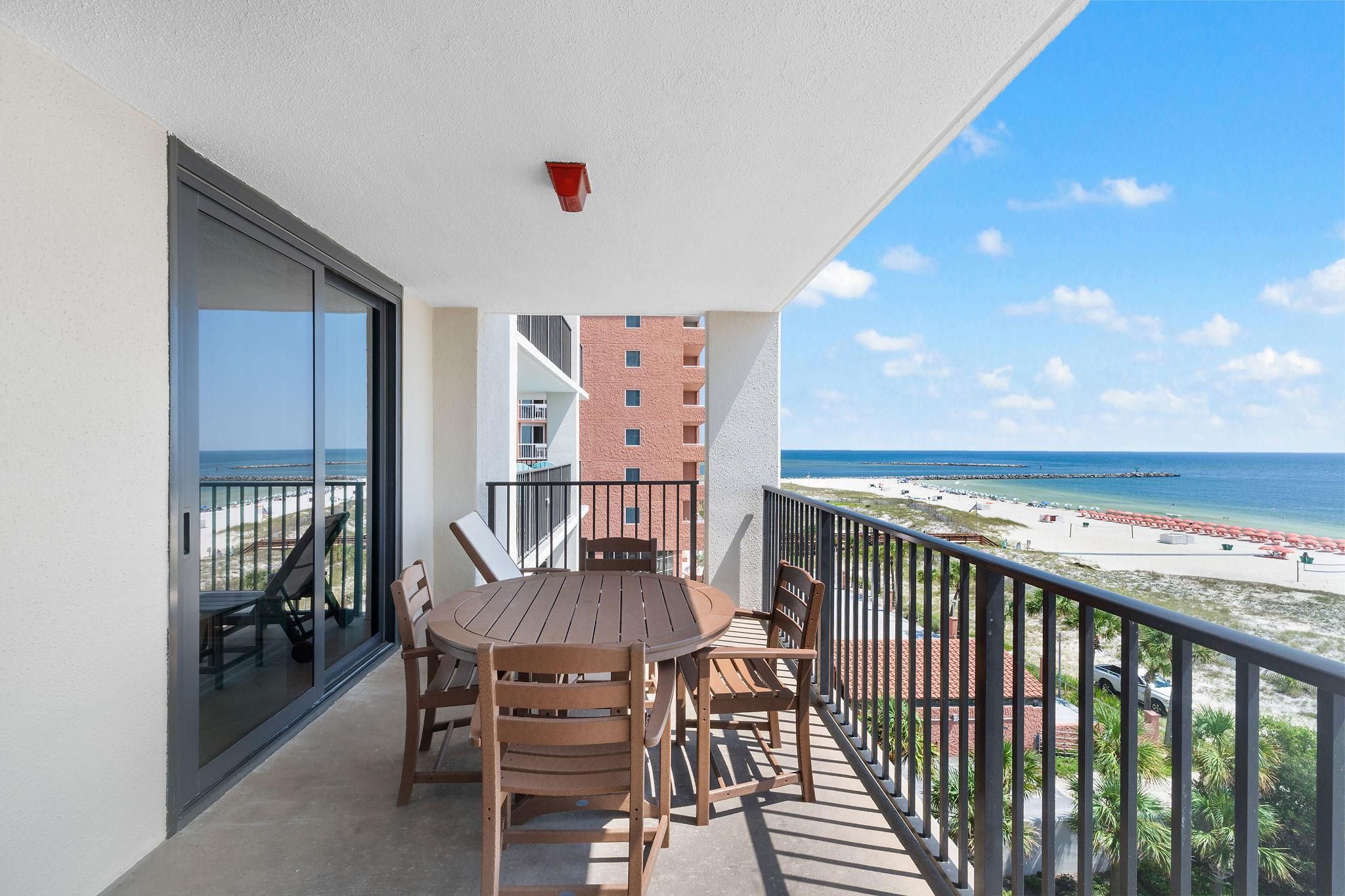 Un balcon avec une table et des chaises, donnant sur une plage et un immeuble.