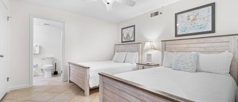 Un dormitorio con dos camas individuales, una cama más grande, un ventilador de techo y un baño visible a través de una puerta abierta.