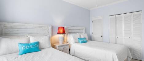 A hotel room with two beds, a ceiling fan, a nightstand with a lamp, and white closets.