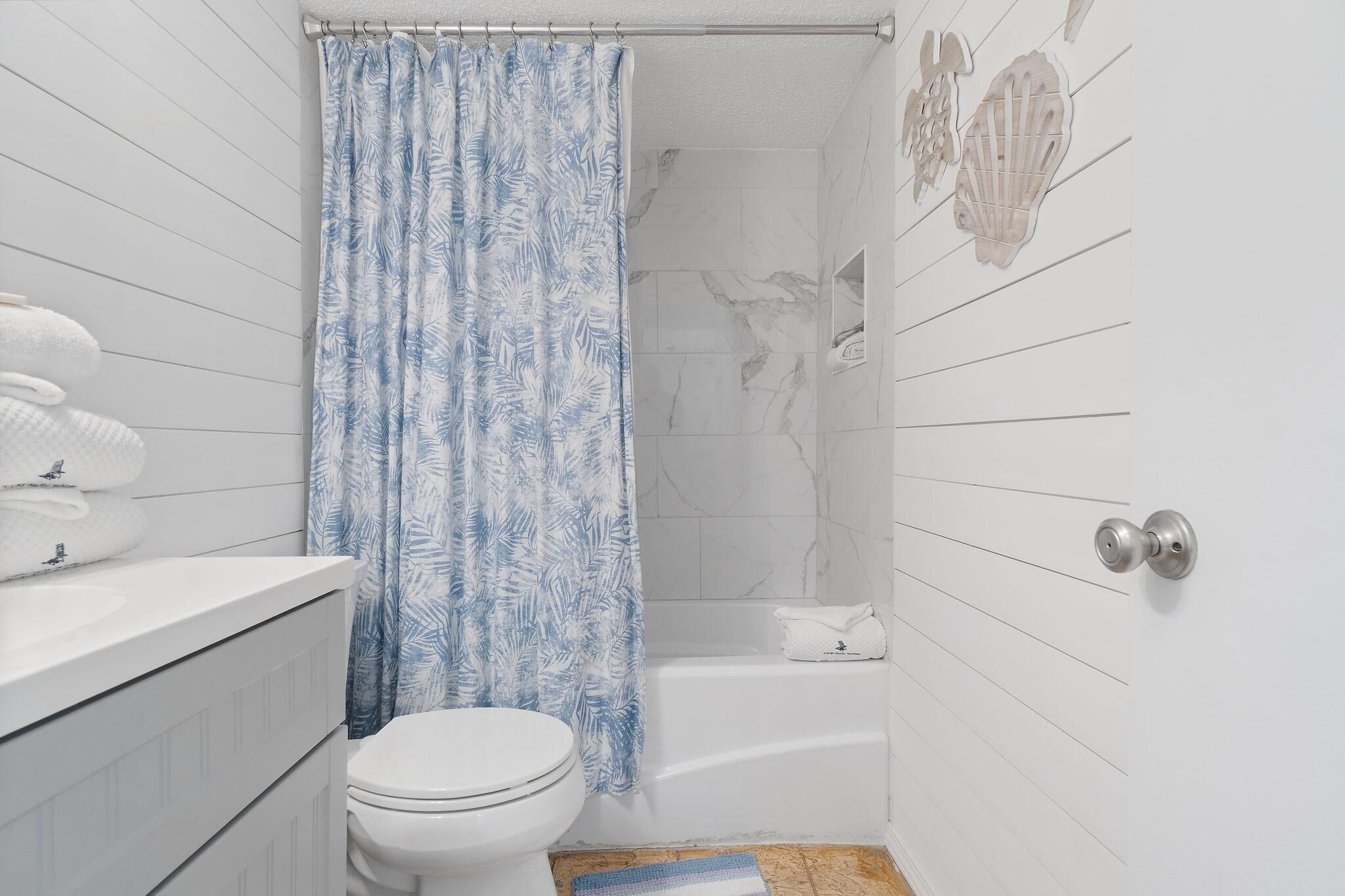 A bathroom with a white toilet, a bathtub, and a shower curtain with a leaf pattern.