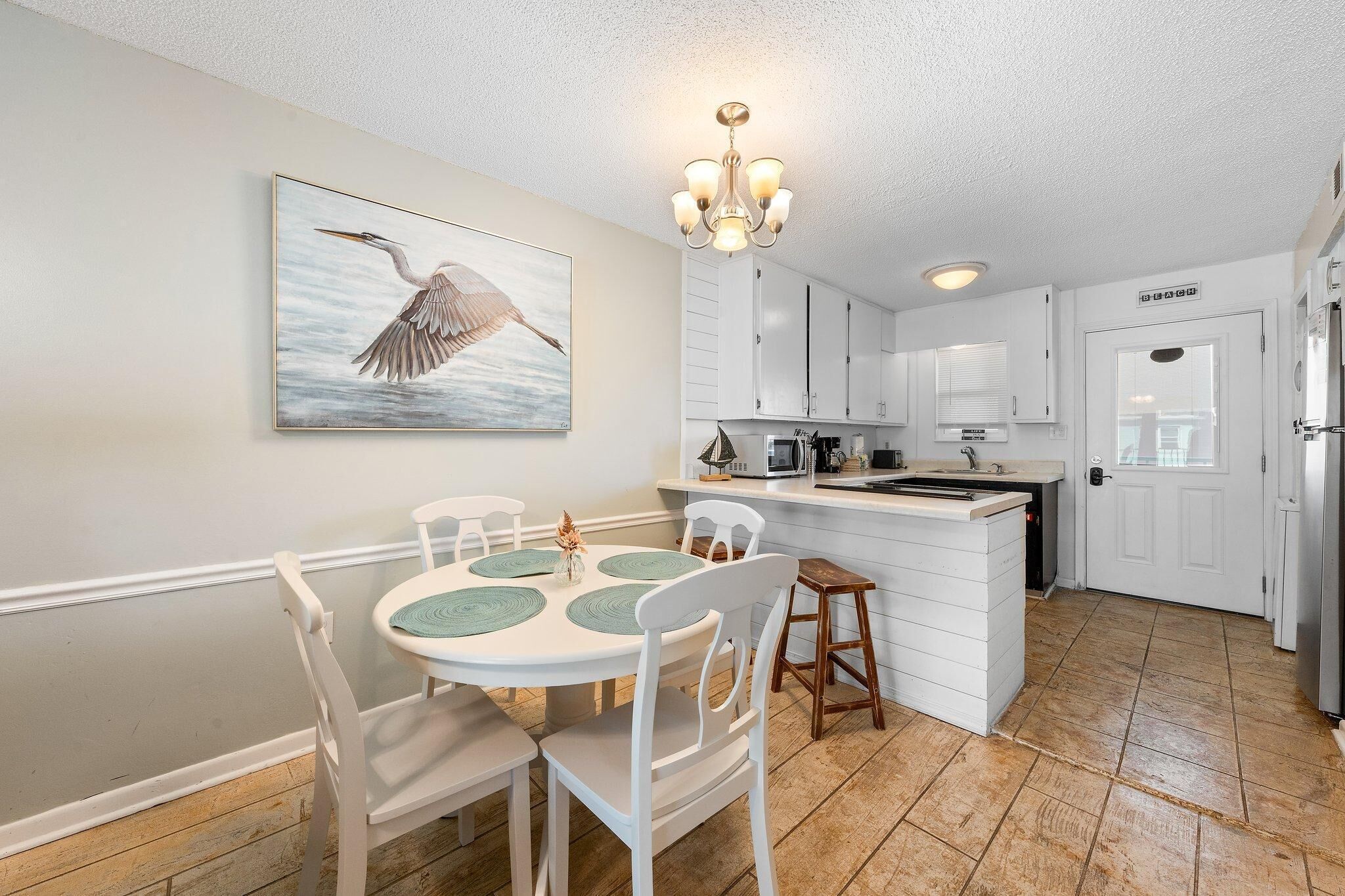 A kitchen with white cabinets, a dining table with white chairs, and a chandelier.