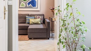 A living room with a grey sofa, patterned cushions, a framed abstract artwork, a small side table with a vase, and a potted plant. - Beatiful design 1 bed apt D (Sevilla)