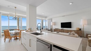 A modern kitchen with a large island, dining area with wicker chairs, a sofa, and a TV. - La Playa 402 (Pensacola)